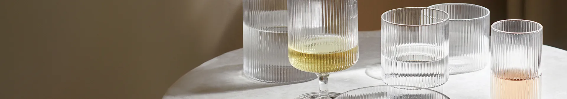 Geribbeld champagneglas met gele vloeistof naast drie geribbelde glazen met heldere en roze vloeistof op een lichte tafel.