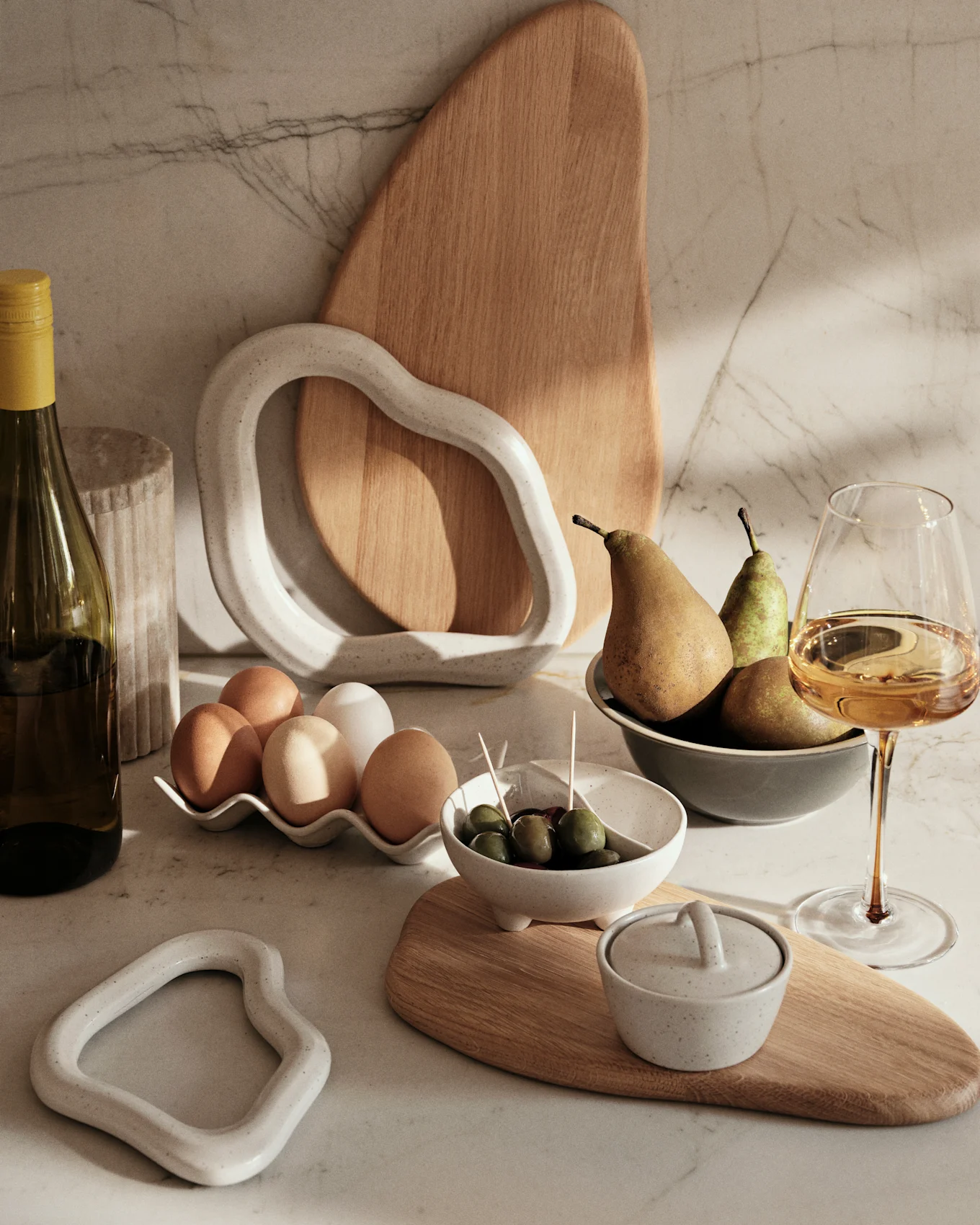 Marmeren aanrecht met wijnfles, eieren, olijven, peren en decoratieve keramische en houten items.