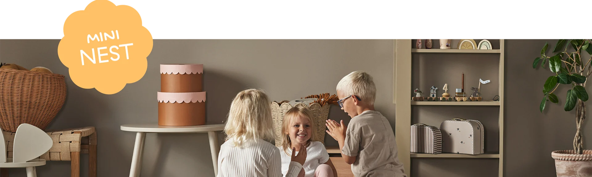 Drie kinderen spelen in een kinderkamer met een speelgoedtrein, decoratieve dozen en een 'MINI NEST'-graphic.