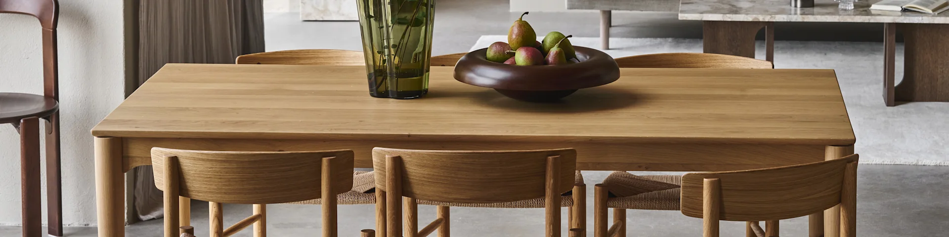 Een houten eettafel met bijpassende stoelen, een groene vaas en een schaal met peren.
