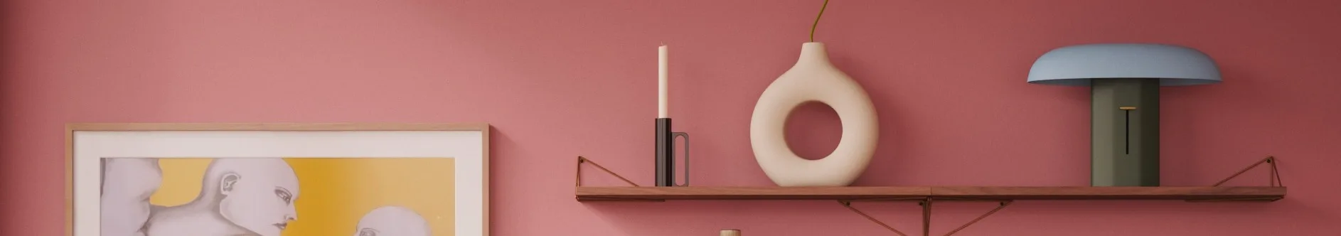 Roze muur, houten plank: witte kaars, crèmekleurige donutvaas met groene stengel, blauwe en groene lamp. Ingelijst kunstwerk links.