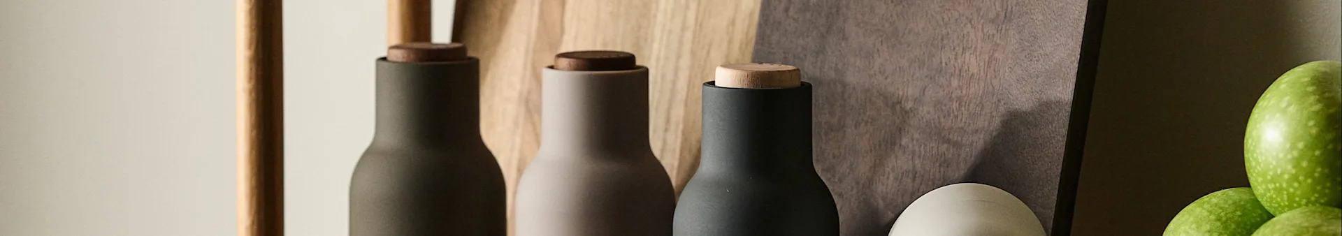 Drie moderne molens in donkergroen, beige en zwart met houten doppen, tegen een houten achtergrond met groene appels.