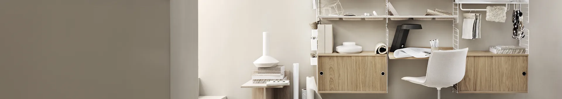 Een minimalistisch thuiskantoor met een wit modulair rekkensysteem, lichte houten kasten en een witte bureaustoel, gevuld met boeken en kantoorbenodigdheden.