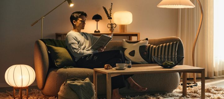 Het kiezen van de juiste lamp is belangrijk voor het gevoel in je huis - een man die op een bank zit, omringd door verschillende lichtbronnen, en een boek leest. 