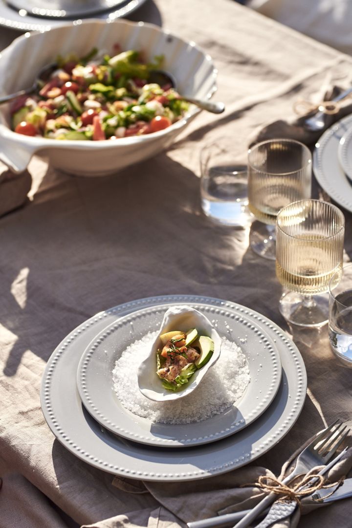 Zomerse bucketlisttip - maak een diner met zeevruchten op de kade met elegant servies op linnen tafelkleden en pallets.