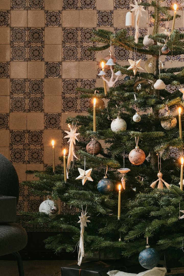 Natuurlijke decoratie-ideeën voor kerstbomen van ferm LIVING. Hier zie je een kerstboom versierd met vilten sterren, bellen en paddenstoelen, allemaal in een kleurenpalet dat de natuur weerspiegelt.