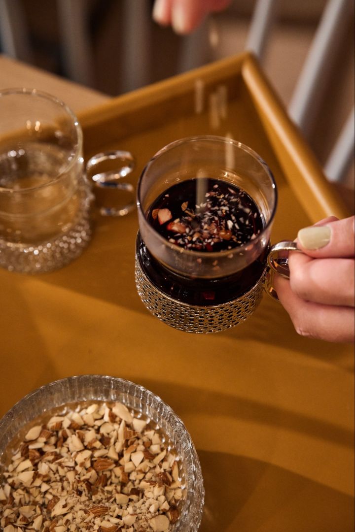 Zweeds kerstdiner: Een hand strooit amandelen in een traditioneel glas glögg op een Scandinavische kersttafel. 