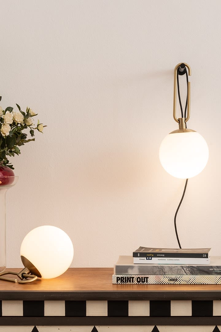 De NH wand- en tafellampen van Artemide hangen en liggen op een bureau met een stapel boeken.