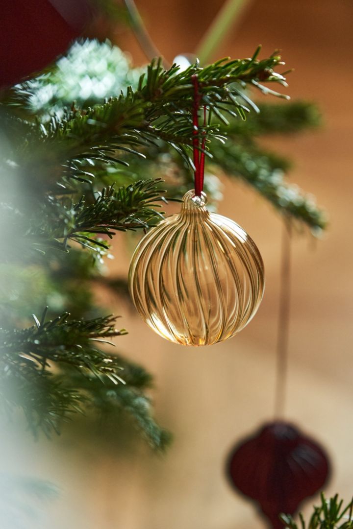 Hier zie je de gouden Clarity-kerstbal van Scandi Living, die schitterend in de boom hangt. Glazen decoraties zijn in 2024 nog steeds net zo geliefd als altijd.