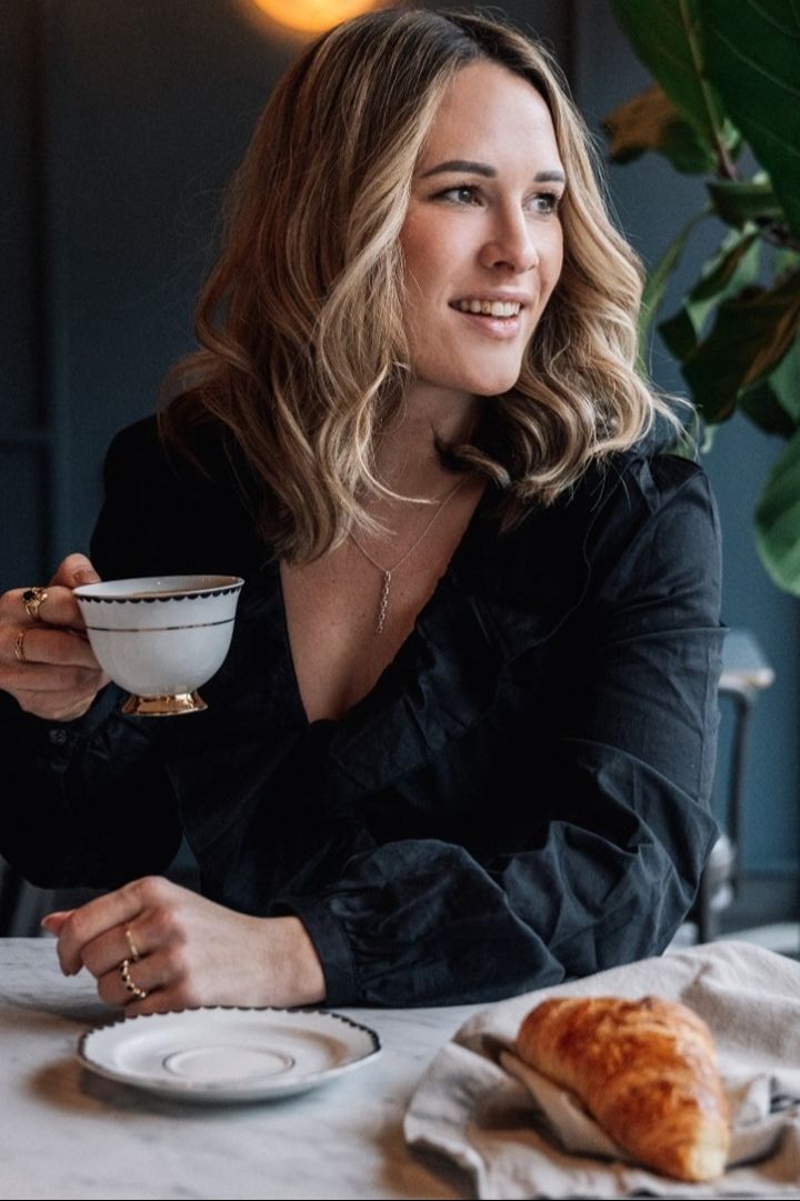 Oprichtster Giovanna Hilke zit aan een tafel en kijkt opzij. Ze houdt de Lignano Sabbiadoro kop van Hilke Collection in haar hand.