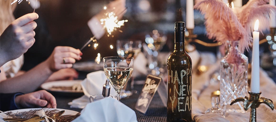 Ideeën voor je nieuwjaarsfeest: Hier zie je een fles versierd met glitterletters op een elegant gedekte tafel.