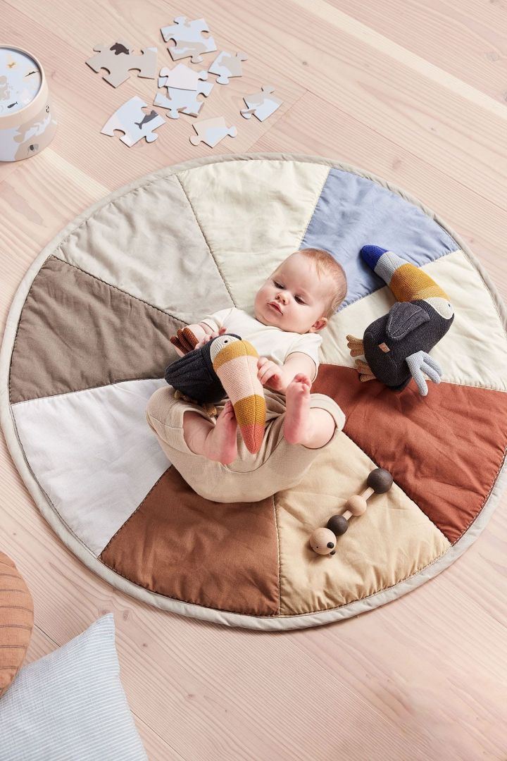 De Trine Toucan knuffel van OYOY ligt naast een baby op het Moni kinderkleed. De knuffel is volledig gemaakt van gerecyclede materialen, wat het niet alleen een geweldig, maar ook een duurzaam cadeau voor een babyshower maakt.