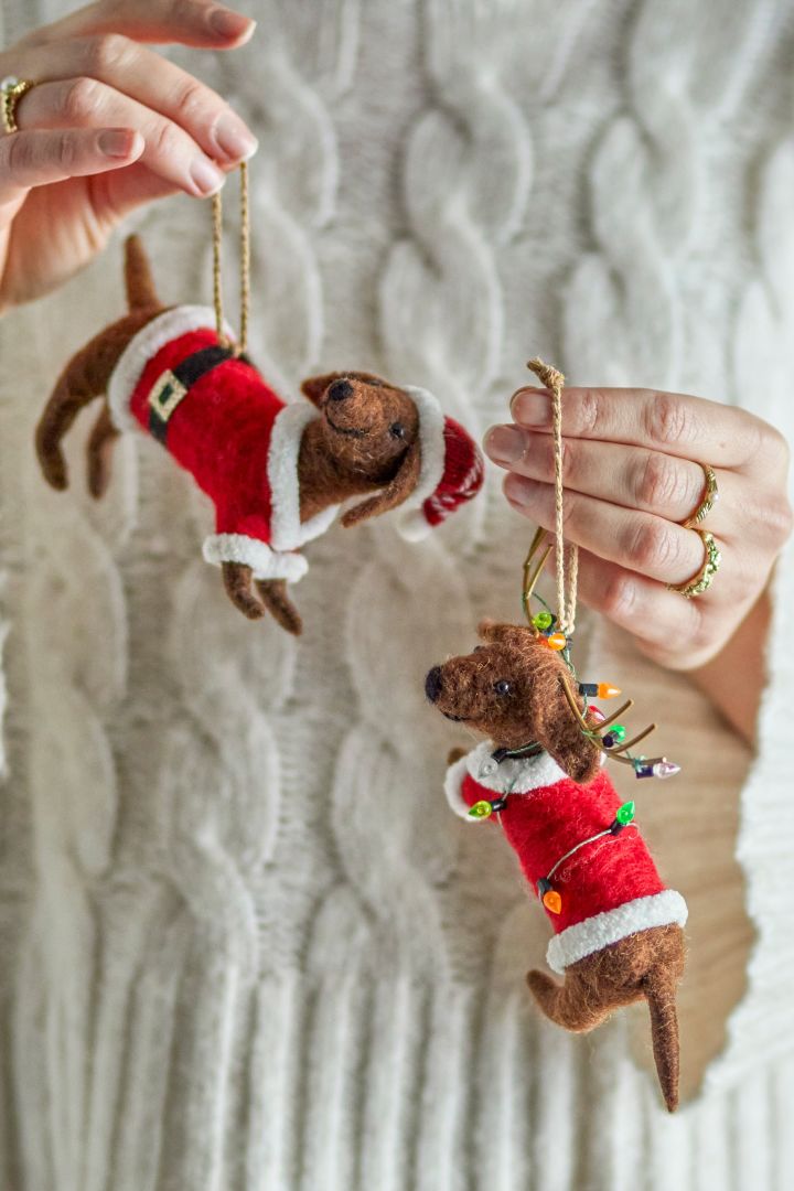 Hier zie je handen die twee vilten hondjes vasthouden, eigenzinnige, speelse kerstboomdecoratie-ideeën.