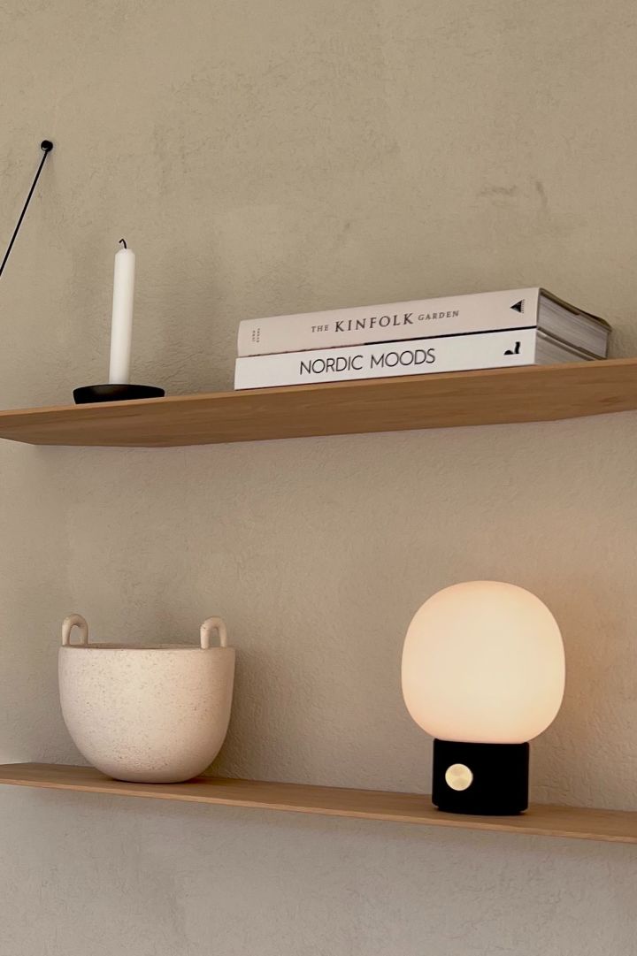 Hier zie je de snoerloze Scandinavische designlamp JWDA in zwart op een plank.