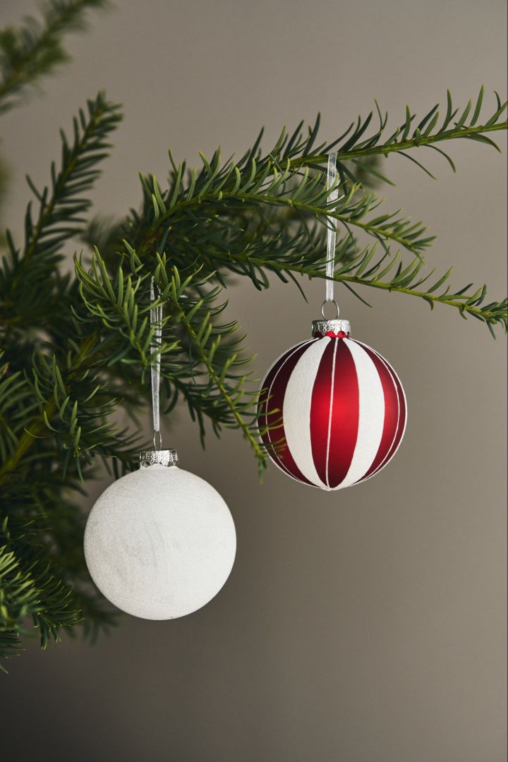 Een rood-wit gestreepte kerstbal van Scandi Living en een witte glitterbal, ook van Scandi Living sieren de kerstboom.