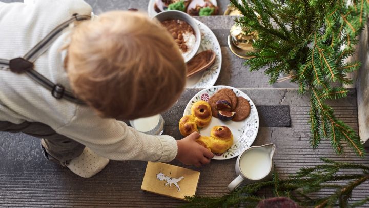 Hier zie je een kind dat naar een Lussekatt grijpt die op een bord uit de Swedish Grace Winter-collectie van Rörstrand ligt.