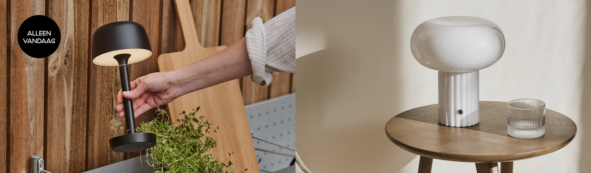 Een hand houdt een zwarte, brandende tafellamp vast, naast een witte paddestoelvormige tafellamp op een houten bijzettafel.