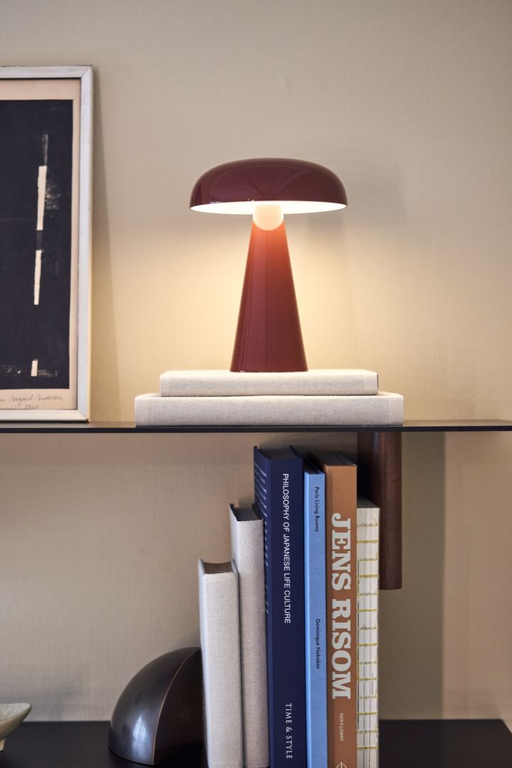 Como draagbare en oplaadbare lamp in rood van &tradition op een stijlvolle boekenplank omringd door boeken. 