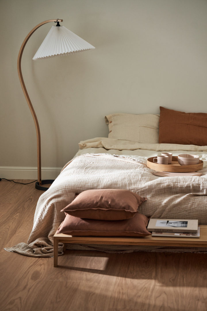 Here you can see a bedroom in Japandi style with a bed, a bench in front of it and the Timberline floor lamp from Gubi next to it.