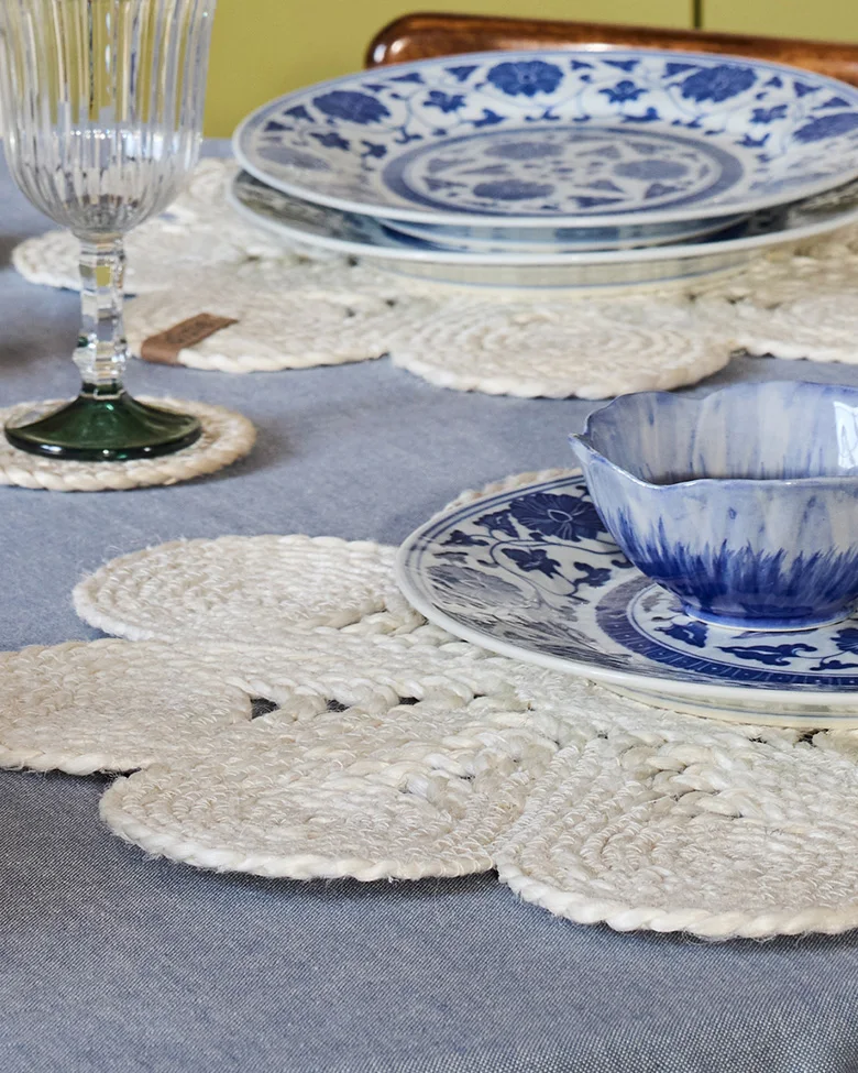 Tafelsetting met blauw-wit servies, witte gevlochten bloemen placemats en een geribbeld glas.