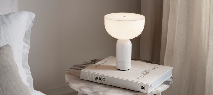 Scandinavische designlampen hebben een onmiskenbare designtaal, zoals duidelijk te zien is in de draagbare Kizu tafellamp die hier op een boek staat.