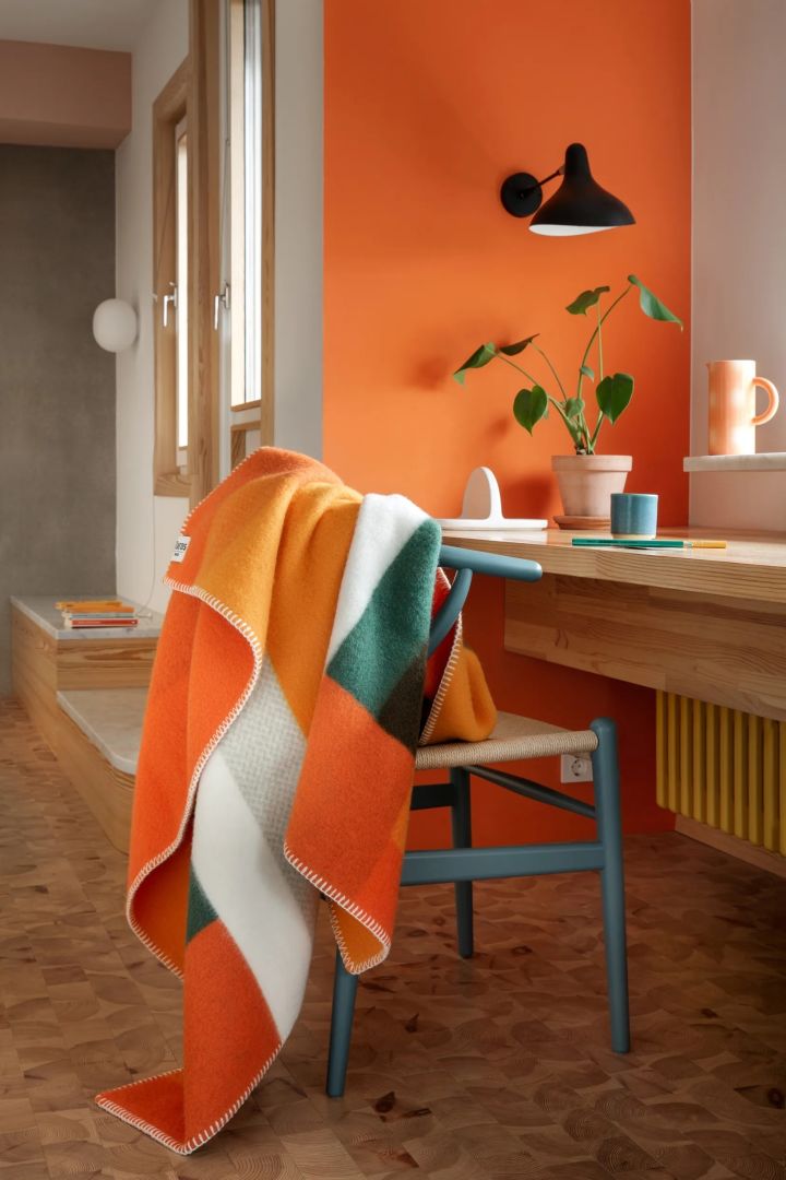 Oranje is een sterke kleur in de interieurtrends 2024. Hier zie je de Mikkel throw in oranje en groen van Røros Tweed.