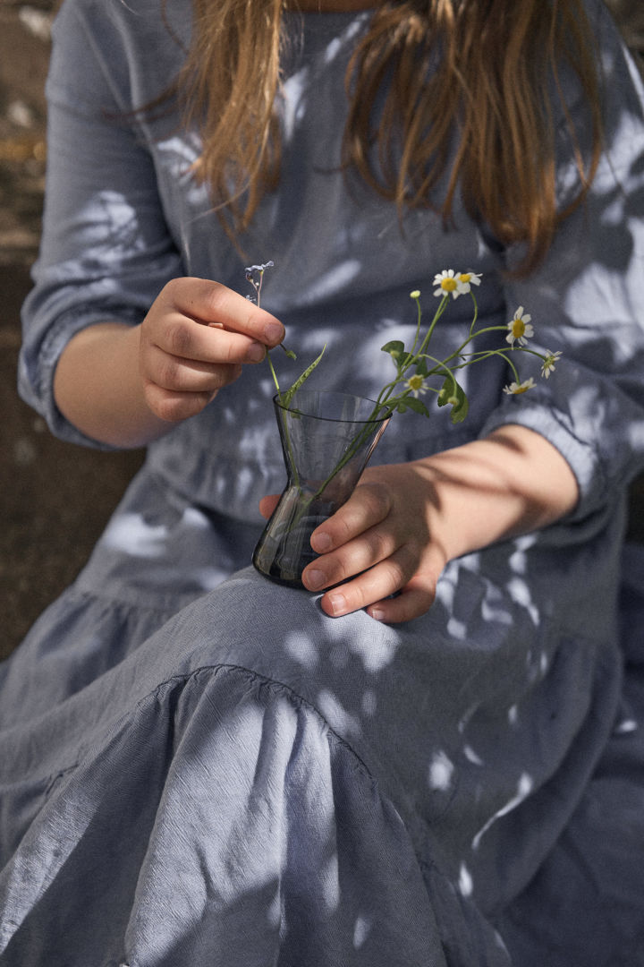 Een midzomertraditie in Zweden is het plukken van bloemen. Hier zie je een meisje in een blauwe jurk met een midzomer vaas met bloemen op haar schoot.