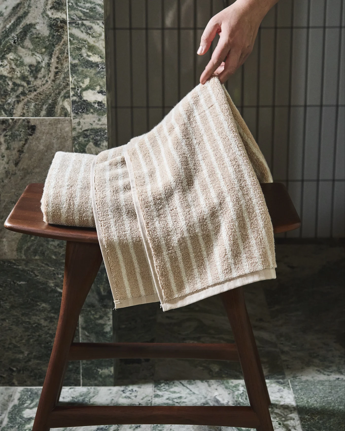 Hand legt een beige-wit gestreepte handdoek op een houten krukje.
