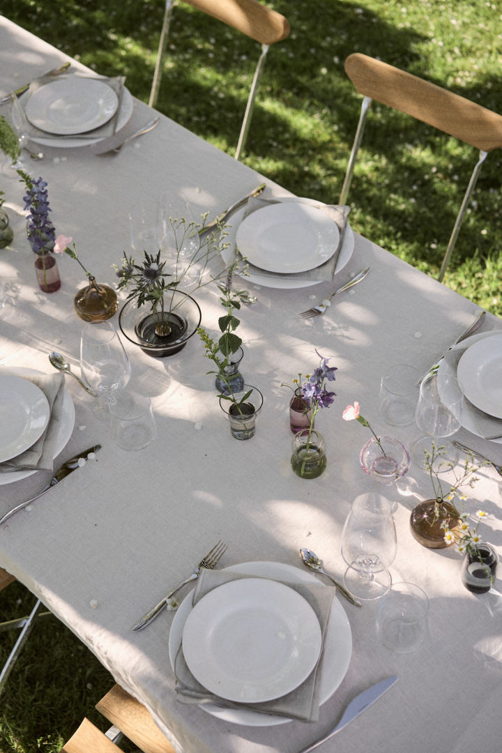 Hier zie je een wit gedekte tafel voor midzomer in Zweden, met de midzomervazen van Orrefors in het midden als blikvanger.