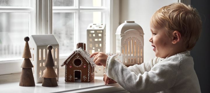 Decoreer met traditionele Scandinavische kerstdecoraties -  Hier zie je een jongetje dat een peperkoekhuisje eet op de vensterbank, omringd door andere kandelaars in de stijl van een peperkoekhuisje.