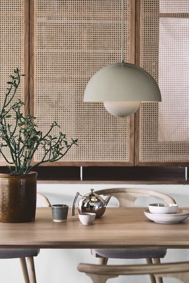 Geniet van de Japandi-trend met eenvoudige, strakke accessoires zoals de VP7 hangende bloempotlamp van &tradition in het grijs. Hier zie je hem hangen in een eetkamer met een rotanwand. 