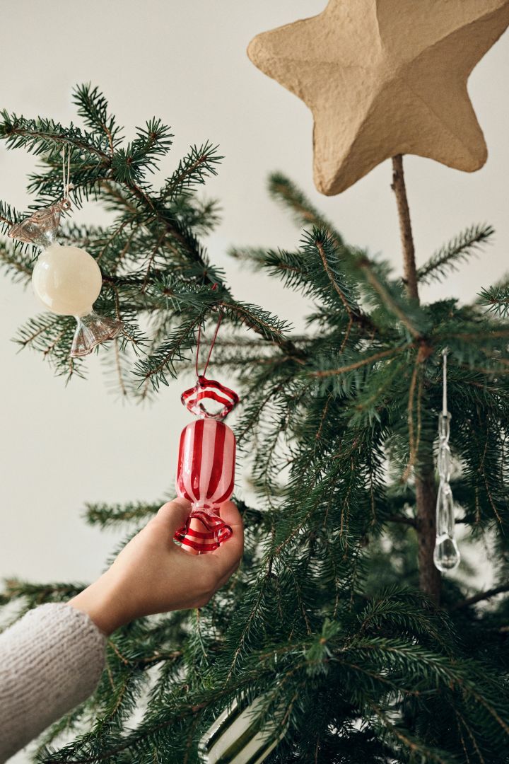 Een hand plaatst een grote ingepakte decoratie snoepje in een kerstboom, een speels en kleurrijk kerstboomdecoratie-idee. 