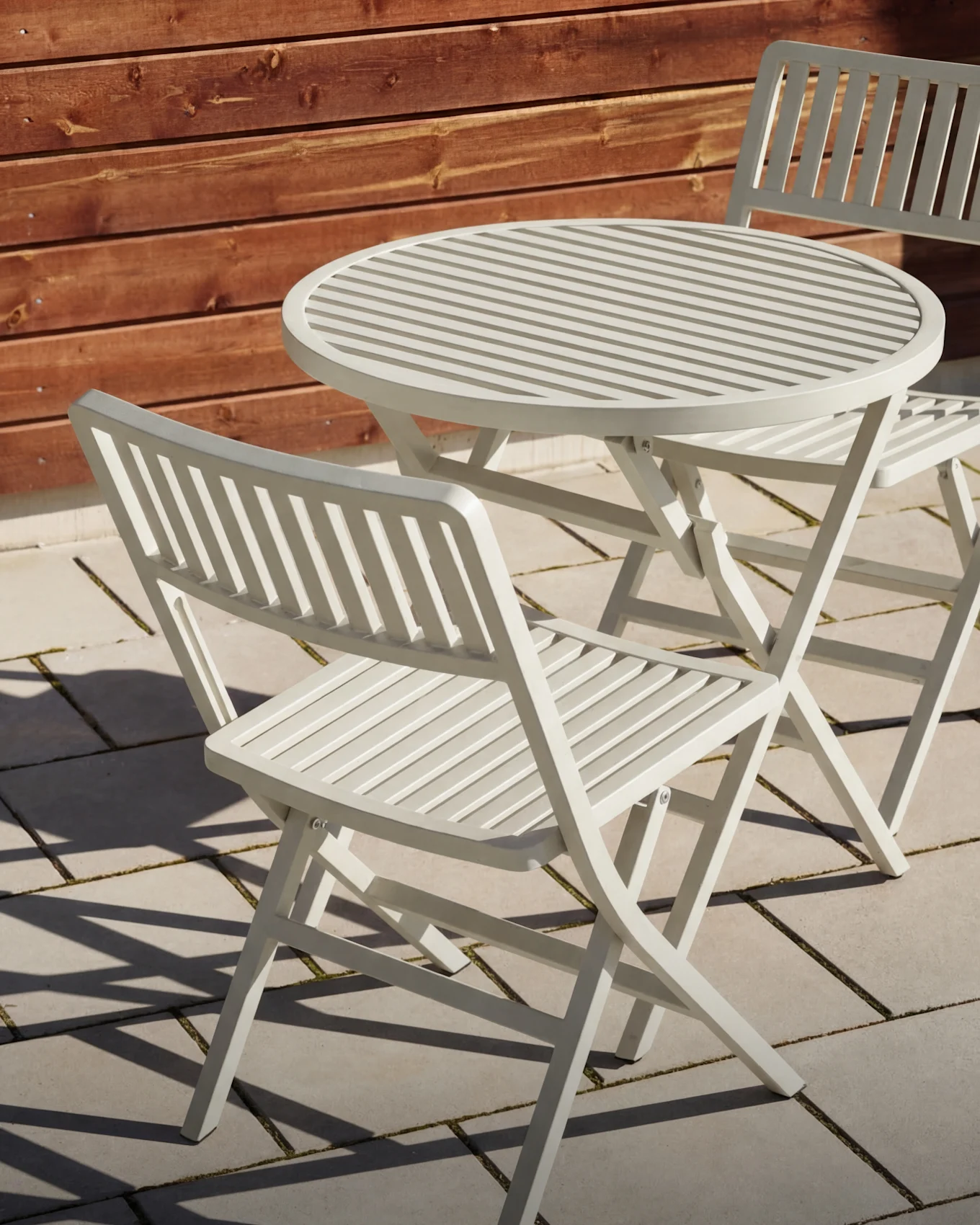 Lichtgrijs latten tuinmeubel met twee bijpassende klapstoelen op een terras.
