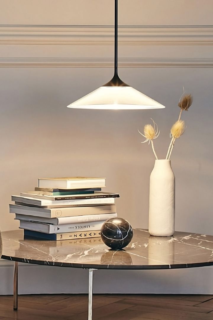 De Orsa-plafondlamp van Artemide hangt boven een tafel met een stapel boeken en een vaas.