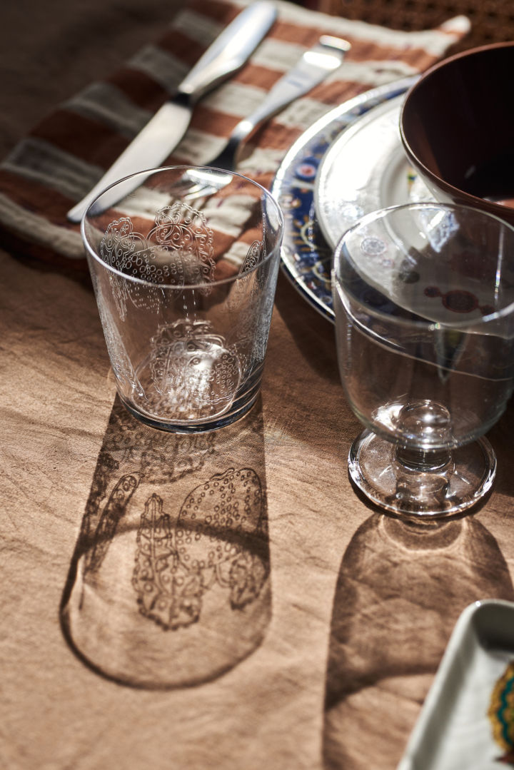 De zon schijnt door het Taika drinkglas en werpt een schaduw op tafel in een bohemien gedekte tafel. 