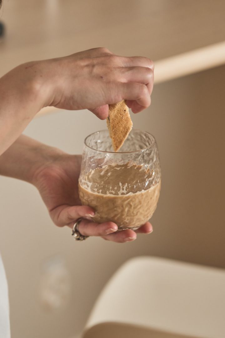 Het Swan glas van Byon is een subtiele knipoog naar de trend van textuurmaterialen in het najaar van 2024. Hier zie je een hand die een koekje in de koffie doopt met het Swan glas.