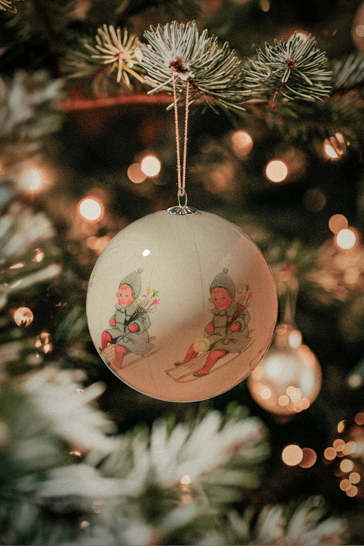 Een close-up van een kerstbal uit de Elsa Beskow-serie van Design House Stockholm, hangend in een sfeervol versierde kerstboom. 