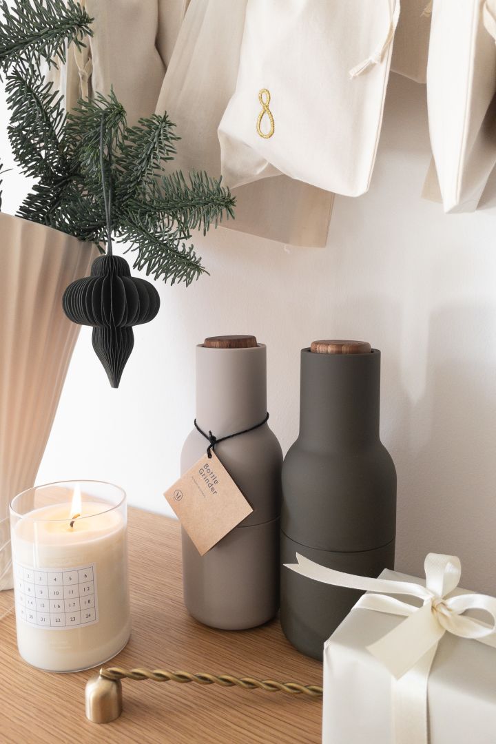 Cadeau-ideeën voor kerst: Geef de Bottle Grinder kruidenmolens van Audo Copenhagen cadeau, die hier te zien zijn op een tafel met een kaars, een vaas met sparrengroen en een adventskalender van Ferm Living.