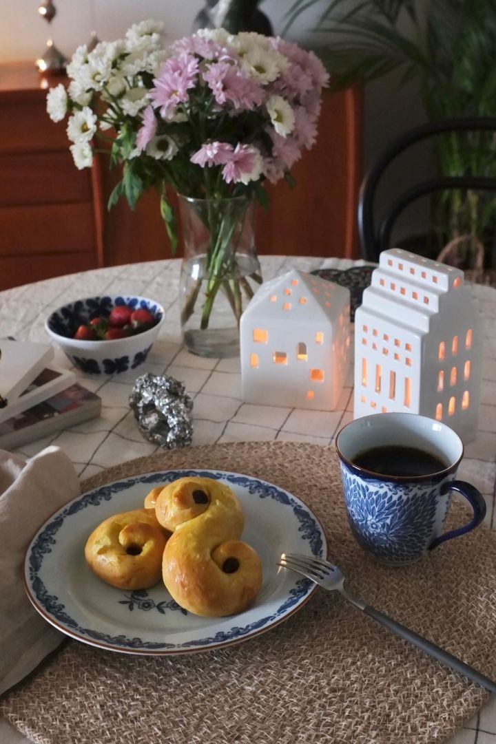 Hier zie je een tafel met verse bloemen en kerstdecoratie in de vorm van Urbania-kandelaren van Kähler en Zweedse Lussekatter op een Ostindia-schotel van Rörstrand in het huis van @_mariano_rivera_4242.