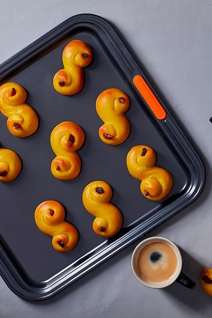 Lussekatter zijn een bijzonder Zweeds gebak dat voornamelijk tijdens de kerstperiode wordt gegeten. Hier zie je heerlijk goudbruin gebakken Lussekatter op een Le Creuset bakplaat.