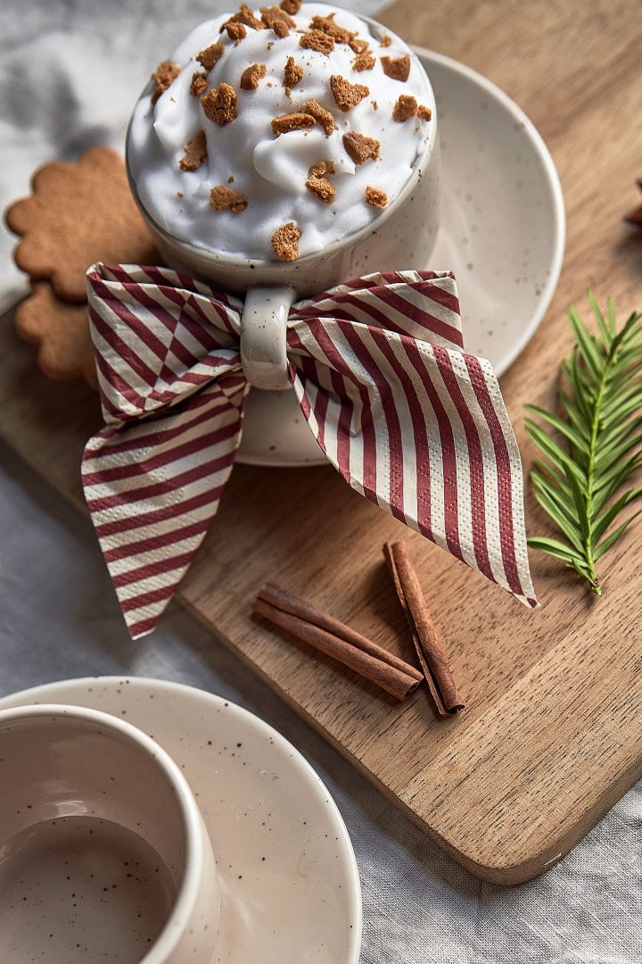 Eenvoudige kerstcocktails: versier je warme chocolademelk of koffie met een topping van slagroom, verkruimelde speculaas en gemalen kaneel. Om te serveren kun je een servet als strik in het handvat draperen.