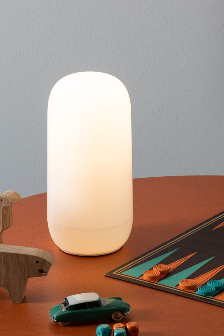 De draagbare Gople-lamp van Artemide staat op een bureau, omringd door houten speelgoed en een backgammonspel.